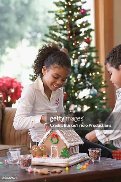 siblings assembling gingerbread house - building a gingerbread house stock pictures, royalty-free photos & images