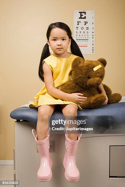 girl sitting on exam table with teddy bear - kind teddy sitzt stock-fotos und bilder