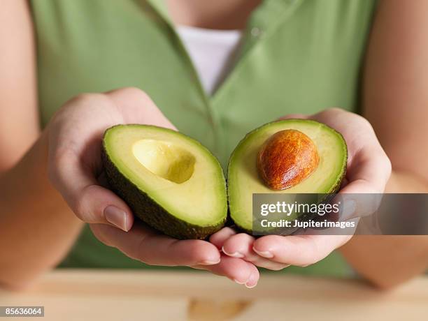 woman holding halved avocado - avocat légume photos et images de collection