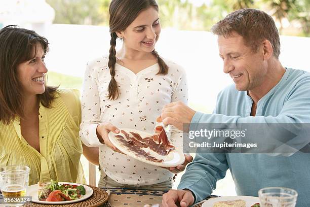 girl offering serrano ham to father - lebensmittel trocknen stock-fotos und bilder