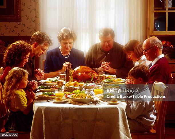 family praying together over thanksgiving dinner - festmahl stock-fotos und bilder