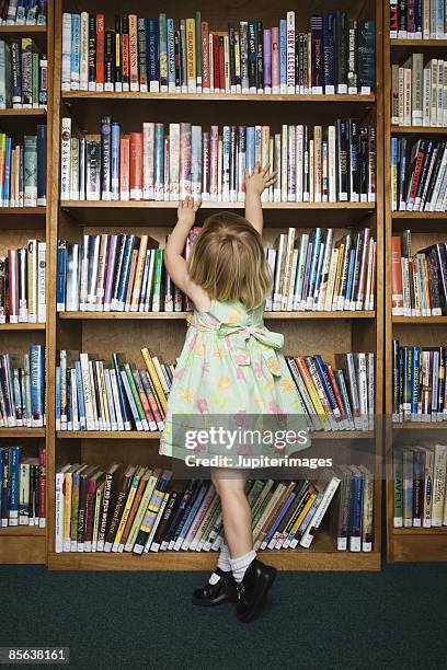 girl in library reaching for book - library kids stock pictures, royalty-free photos & images