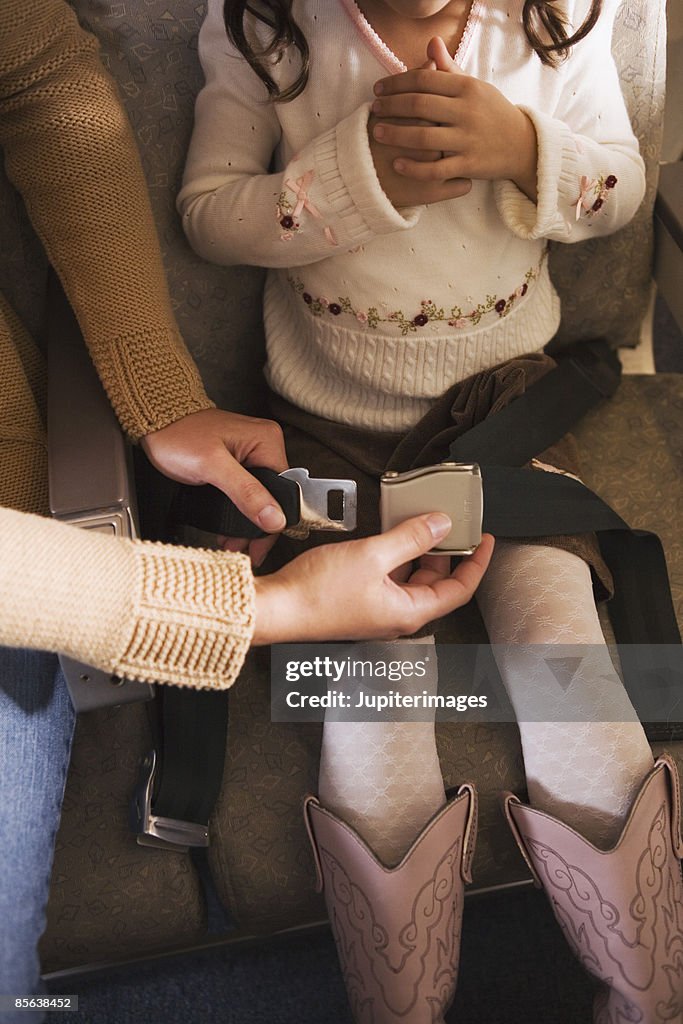 Mother adjusting child's seatbelt on airplane
