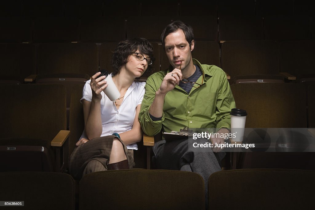 Man and woman sitting in theater conducting casting call,25-30 years,30-35 years,adult,audition,auditorium,beverage,bohemian,brunette,casting,casting call,casting director,casual attire,caucasian,cinema,clipboard,coffee