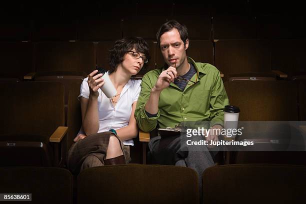 man and woman sitting in theater conducting casting call,25-30 years,30-35 years,adult,audition,auditorium,beverage,bohemian,brunette,casting,casting call,casting director,casual attire,caucasian,cinema,clipboard,coffee - critics - fotografias e filmes do acervo