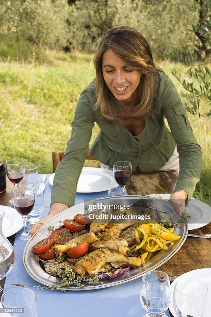 Woman passing grilled chicken and vegetables platter