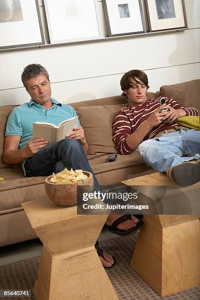 father reading and son text messaging - couch opposites stock pictures, royalty-free photos & images