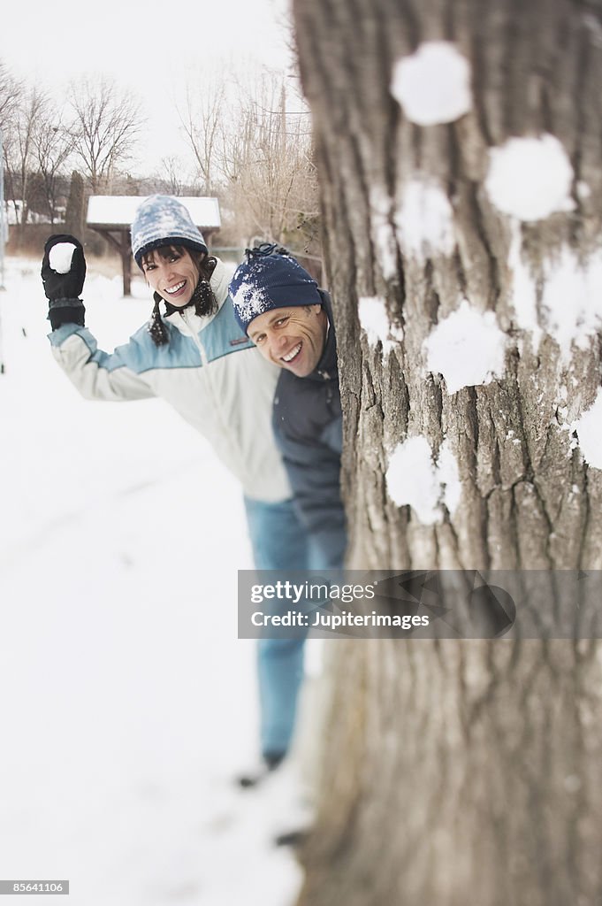 Couple hiding behind tree in snowball fight