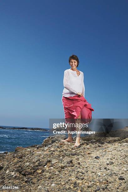 woman walking on rocky beach - older women in short skirts stock pictures, royalty-free photos & images