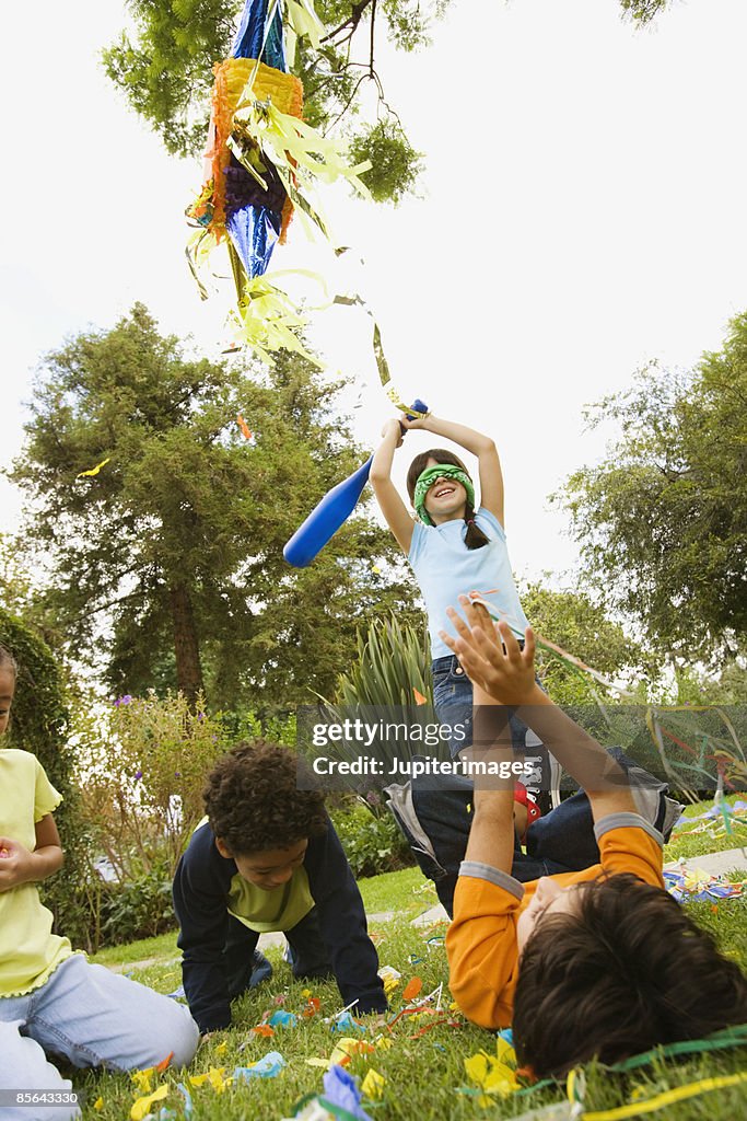 Girl hitting pinata at birthday party and children grabbing candy