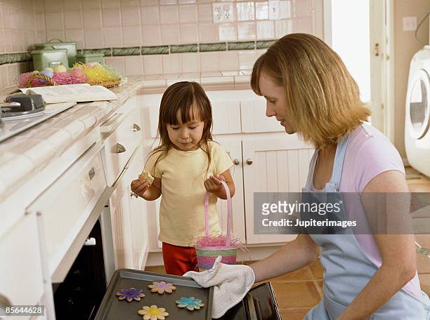 daughter watching mother remove cookies from oven - hot filipina women stock pictures, royalty-free photos & images