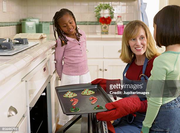girls watching woman take cookies out of oven - hot filipina women stock pictures, royalty-free photos & images