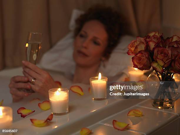 woman relaxing in bathtub with champagne - candle light foto e immagini stock