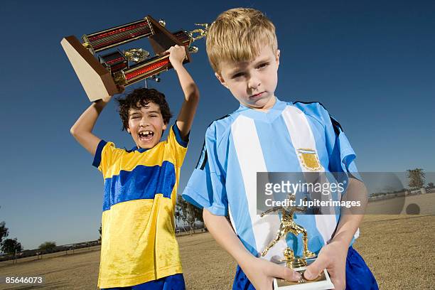 winner and loser holding soccer trophies - second place fotografías e imágenes de stock