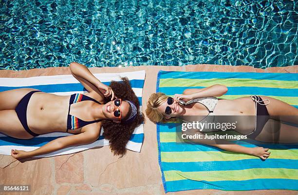 friends with cell phones sunbathing beside pool - girls sunbathing stock-fotos und bilder