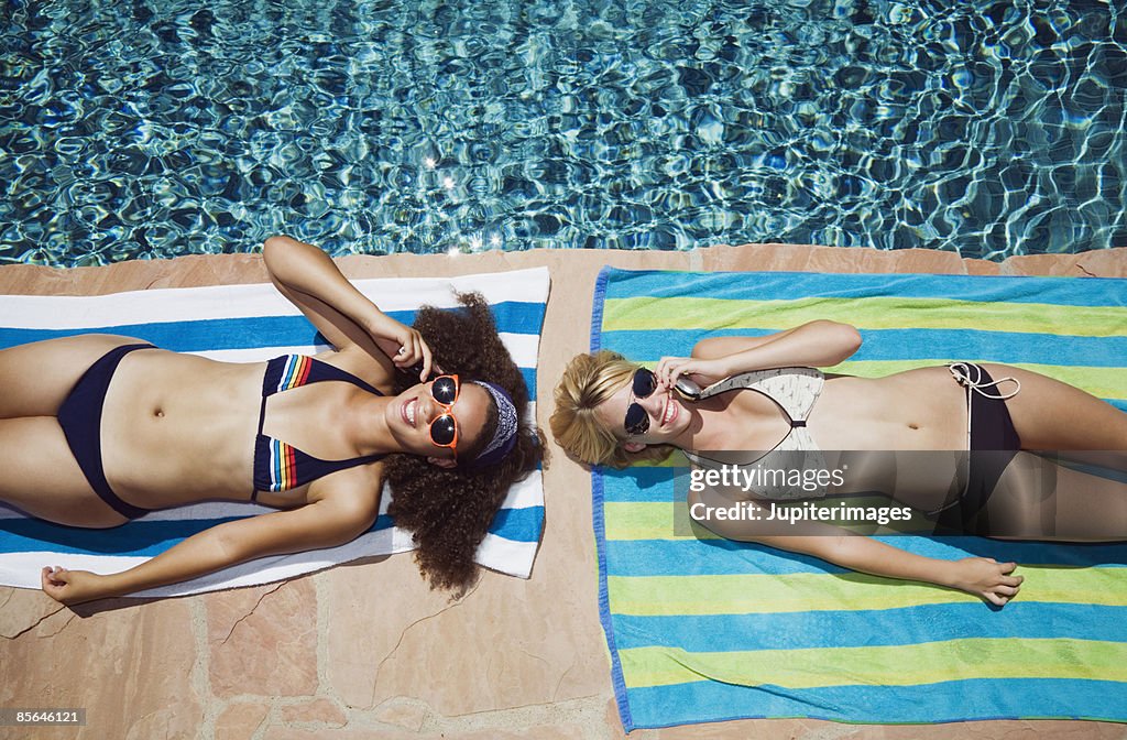 Friends with cell phones sunbathing beside pool