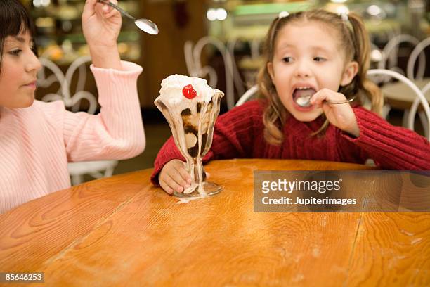 girls eating overflowing hot fudge sundae - filet de caramel photos et images de collection