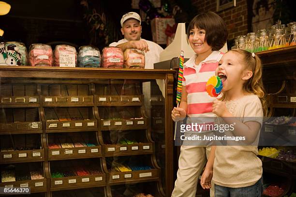 girls holding colorful lollipops in candy shop - lollipop man stockfoto's en -beelden