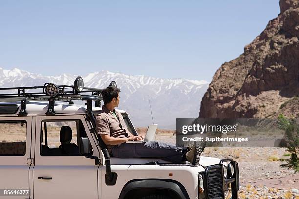 man with laptop computer sitting on vehicle, mendoza, argentina - 起伏の多い地形 ストックフォトと画像
