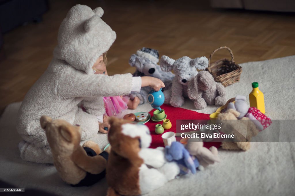 Child in cozy hooded bear costume, having a tea party with teddies and dolls