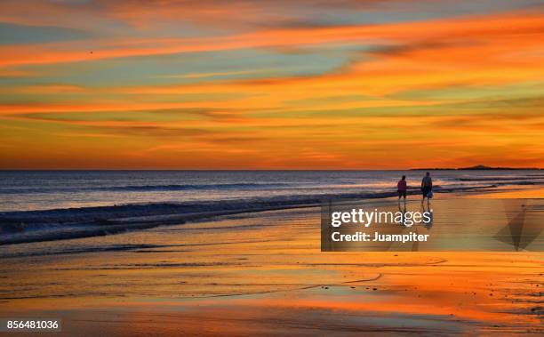 pareja caminando por la orilla durante un espectacular atardecer - pareja en la playa stockfoto's en -beelden