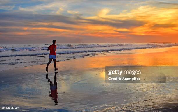 un corredor solitario en la orilla de la playa durante un espectacular atardecer - juampiter fotografías e imágenes de stock