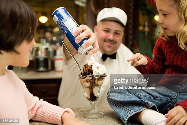 man topping hot fudge sundae with whipped cream - サンデー ストックフォトと画像