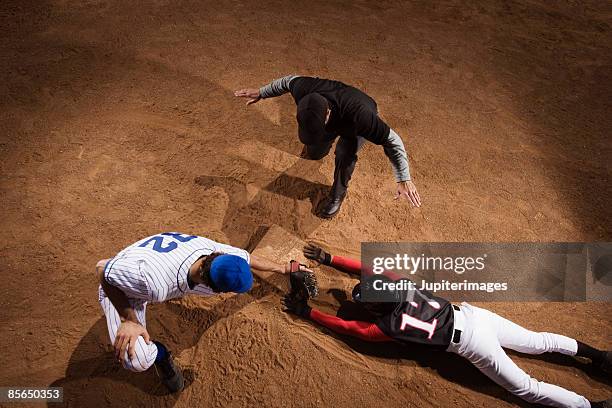 baseman trying to strike out baseball player while umpire signals him safe - baseball umpire stock pictures, royalty-free photos & images