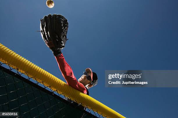 baseball player leaning over fence to catch baseball - luva roupa desportiva de proteção imagens e fotografias de stock
