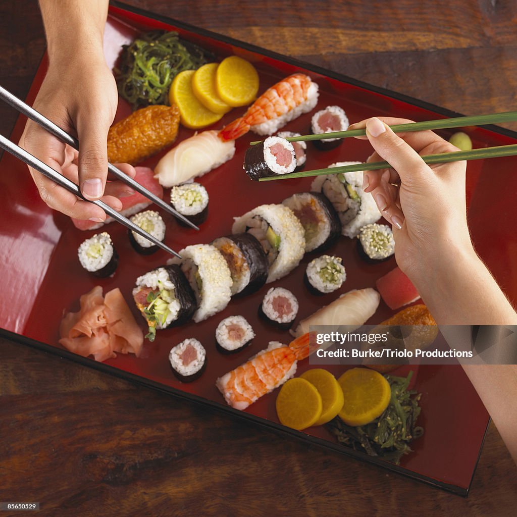 Hands eating sushi with chopsticks