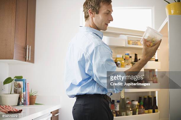 man looking at leftovers in refrigerator - leftovers stockfoto's en -beelden