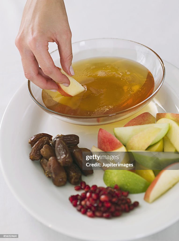 Hand dipping apple into honey with Rosh Hashanah fruit plate