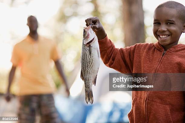 boy at campsite holding fish - kids fishing stock pictures, royalty-free photos & images