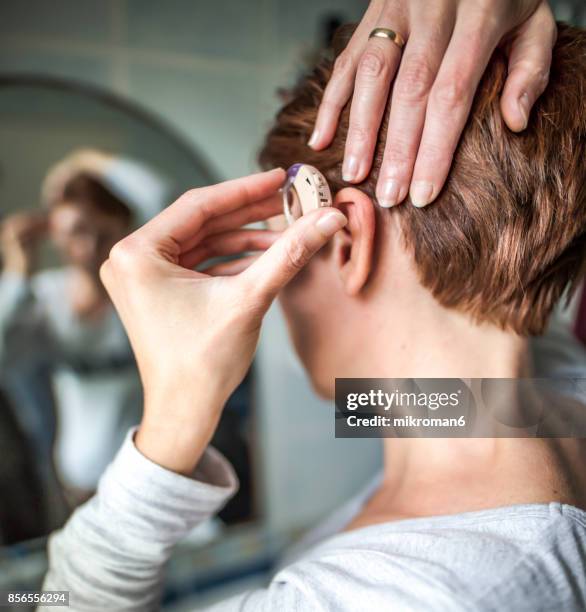 women inserting hearing aid. medical concept - problemas de audición fotografías e imágenes de stock