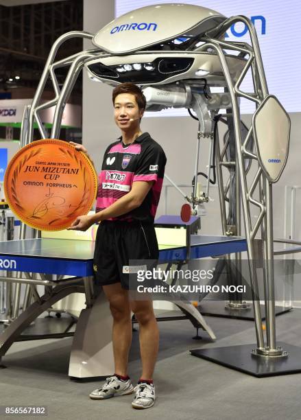 Japan's Olympic medallist Jun Mizutani poses with FORPHEUS, a fourth-generation table-tennis robot developed by automation parts maker Omron, during...