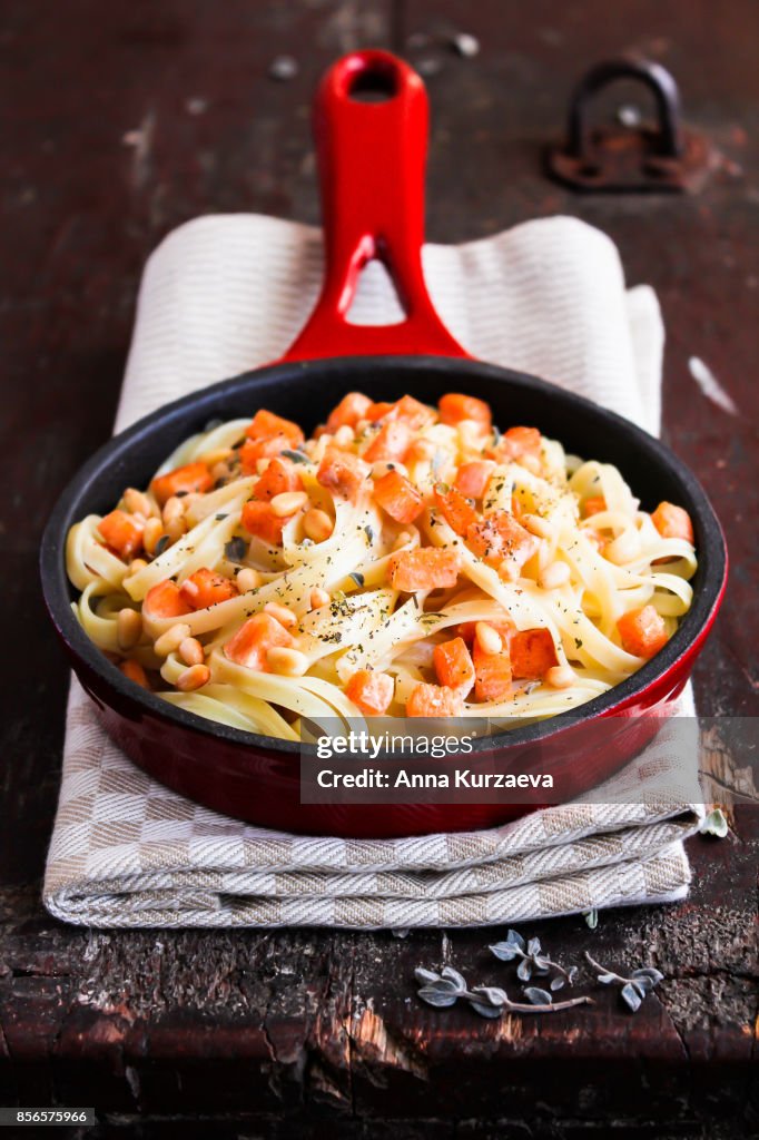 Homemade noodles with roasted salmon or trout fish, cream sauce, pine nuts and herbs in a pan on a wooden table, selective focus