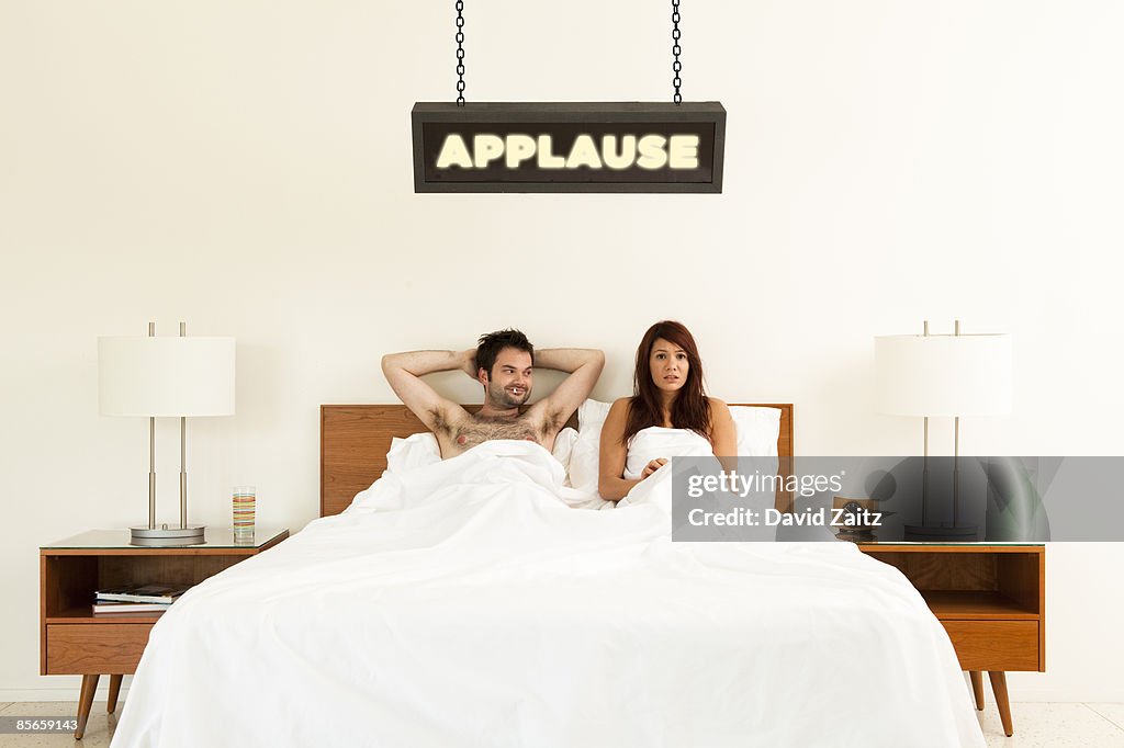 Man and woman in bed under "Applause" sign