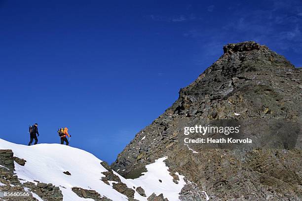 two men climbing snowy peak. - glacier national park montana stock pictures, royalty-free photos & images