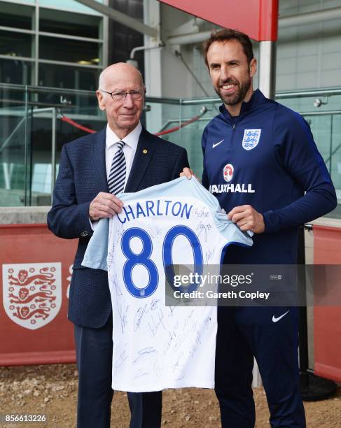 Sir Bobby Charlton is presented with a signed shirt by Gareth Southgate manager of England as a pitch is named in his honour during an England...