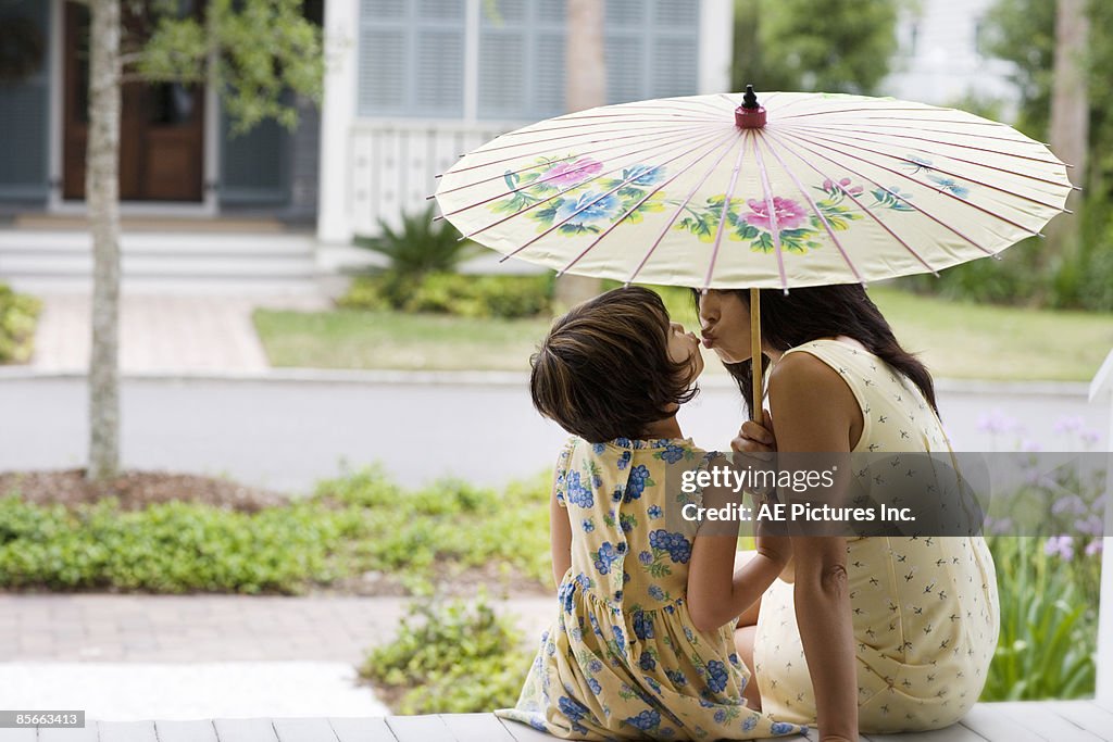 Mother and daughter kiss under umbrella