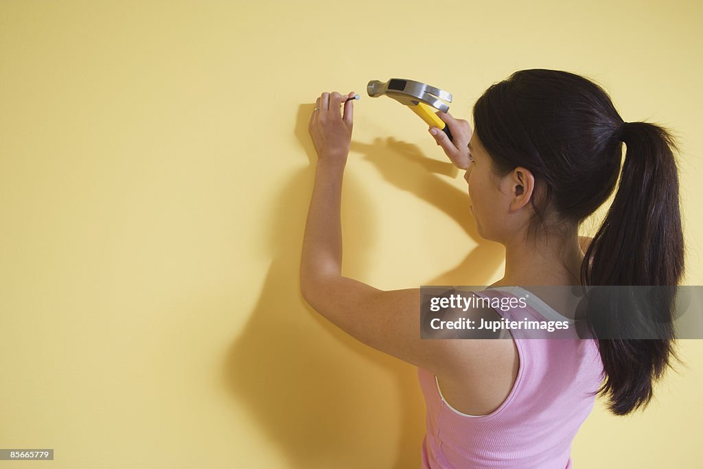 Woman hammering nail in wall
