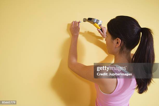 woman hammering nail in wall - hamer stockfoto's en -beelden