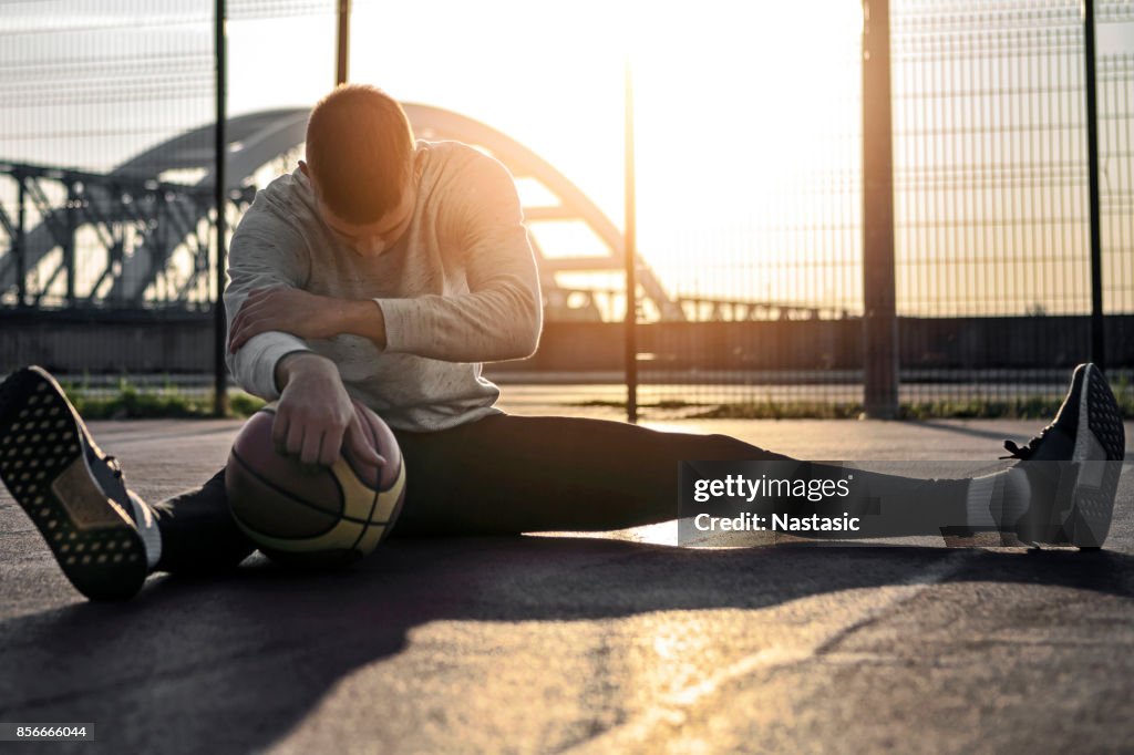 Man die zich uitstrekt voordat basketbalspel met ochtendzon op achtergrond