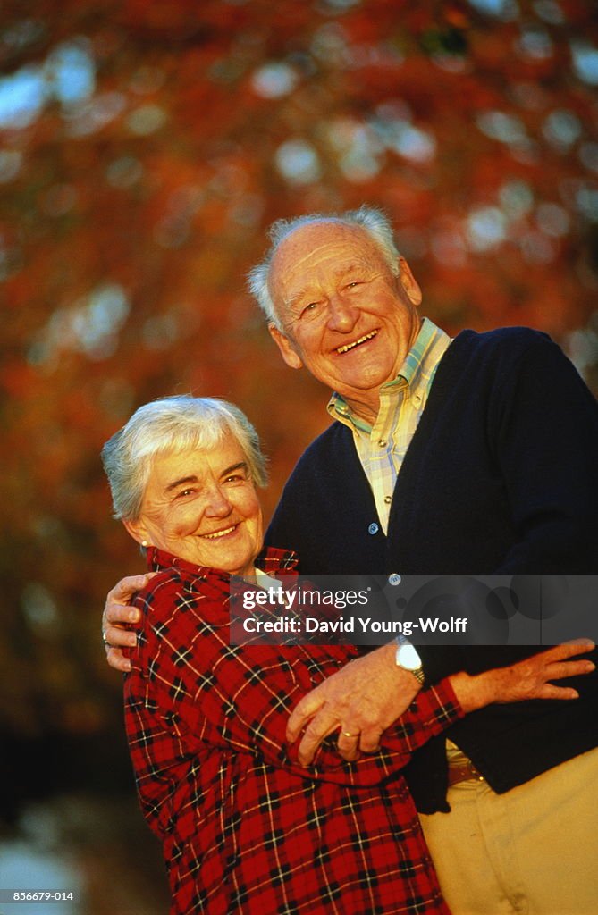 Elderly couple standing outdoors, autumn trees in background