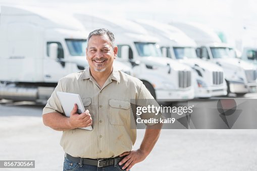Hispanic man standing in front of semi-trucks Hispanic man standing in front of semi-trucks