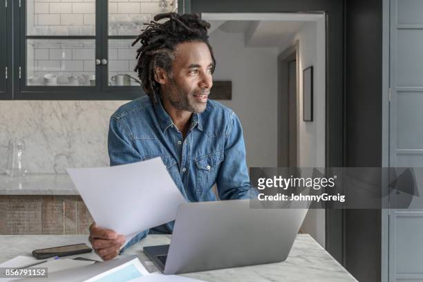 vertrouwen zakenman in zijn 50s thuiswerken met laptop en papierwerk - dreadlocks stockfoto's en -beelden