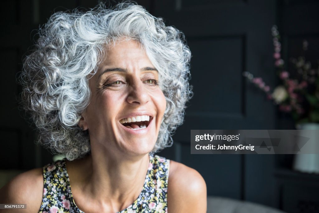 Woman with grey curly hair looking away and laughing