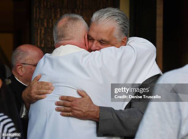 Clark County Commission Chair Steve Sisolak embraces a member of the clergy as he attends a vigil at Guardian Angel Cathedral for the victims of the...