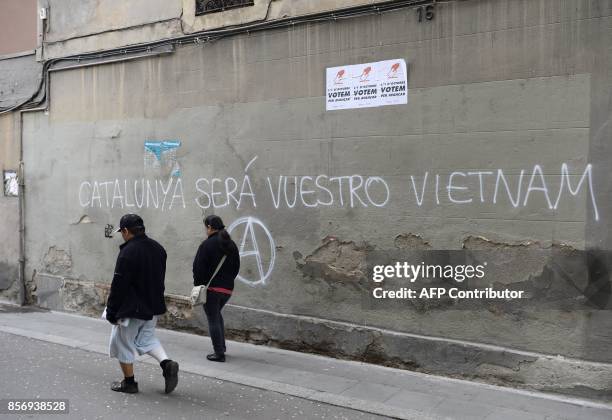 Two people walk in front of a graffiti reading "Catalonia will be your Vietnam" in Barcelona, on October 3, 2017. Large numbers of Catalans are...