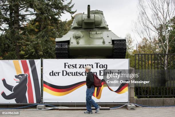 Man is passing by a sign reading 'Festival of the Day Of German Unity' and a T-34 Tank part of the Soviet Soldier monument near by an amusement area...